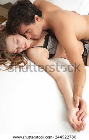 Over head close up view of a young attractive couple laying in bed at home, in an intimate sensual loving moment. Man and woman enjoying sex together in a hotel room, beauty and lifestyle.