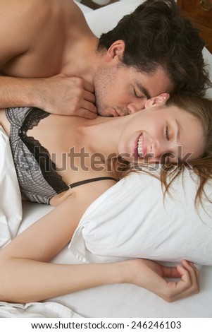 Close up portrait of a young attractive romantic couple hugging and kissing, laying down on a white bed, having sex and loving each other, smiling. Love and relationships lifestyle, interior bedroom.