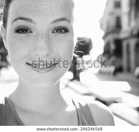 Black and white portrait of attractive young smiling tourist woman visiting a sunny destination city with the sunshine filtering through her on a summer holiday trip. Travel and smart lifestyle.