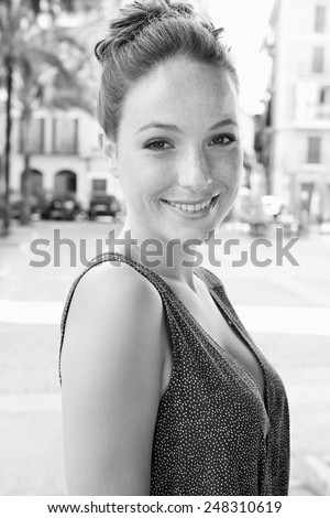 Black and white close up portrait of a young and beautiful tourist woman visiting a destination city on holiday. Travel and tourism. Sophisticated woman elegantly smiling looking at camera, outdoors.