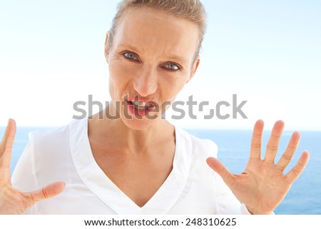 Close up beauty portrait of angry furious woman arguing with a strong feelings against a blue sky and sea background. Feeling and emotions in lifestyle living life. Gestures and expressions outdoors.