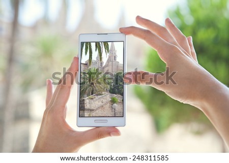 Close up detail view of a young tourist woman hands holding a smartphone mobile cell device, taking pictures of a monument while sightseeing on a holiday trip. Travel and technology outdoors.