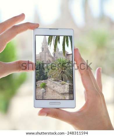 Close up detail view of a young tourist woman hands holding a smartphone mobile cell device, taking pictures of a monument while sightseeing on a holiday trip. Travel and technology outdoors.