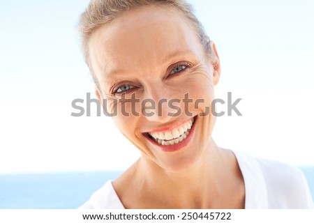 Close up beauty portrait of happy and joyful woman showing a fun and carefree expression of joy against a blue sky and sea background. Feelings and emotions in lifestyle. Gestures and expressions.