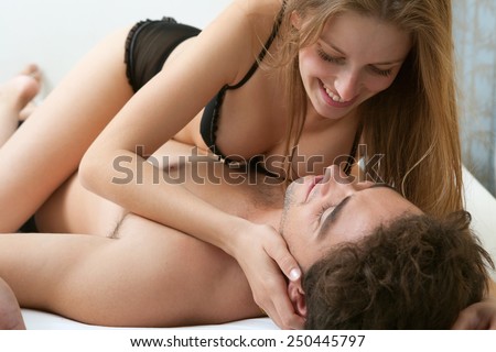 Young and attractive couple being playful and intimate, enjoying having sex in a white bedroom in a hotel, wearing underwear and smiling. Relationships, sex and emotions. Lifestyle, home interior.