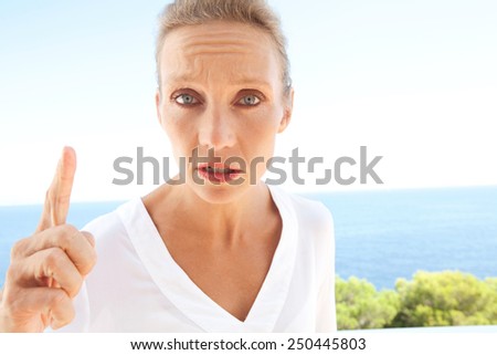 Close up beauty portrait of angry woman arguing and telling off using her finger against a blue sky and sea background. Feelings and emotions in lifestyle living. Gestures and expressions outdoors.