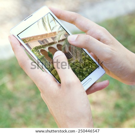 Close up detail view of a young tourist woman hands holding and using a touch screen smartphone mobile device, flicking through holiday pictures on vacation. Travel and lifestyle technology.