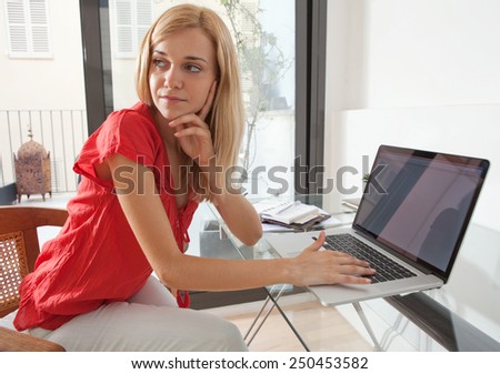 Portrait of a young professional woman being thoughtful in her home office space, turning away. Student girl using a laptop computer at her home work desk. Lifestyle and technology, interior.