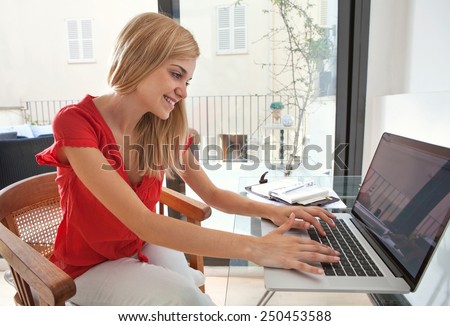 Portrait of young professional woman smiling in her home office space, typing and working at her desk. Student girl using a laptop computer at her home work table. Lifestyle and technology, interior.