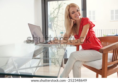 Attractive and friendly young professional woman joyfully smiling in home office space, smiling. Student girl using a laptop computer at her home work desk. Lifestyle and technology, interior.
