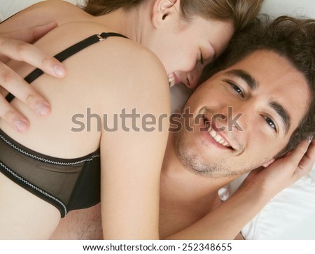 Close up portrait of attractive young couple hugging and caressing in a hotel bed being in love, wearing a black bra, playful in a bedroom. Love, passion and romance lifestyle, home interior.