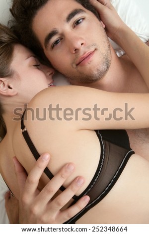 Overhead close up portrait of a young romantic couple hugging laying down on a bed with their heads together, loving each other. Love and relationships lifestyle, interior bedroom.