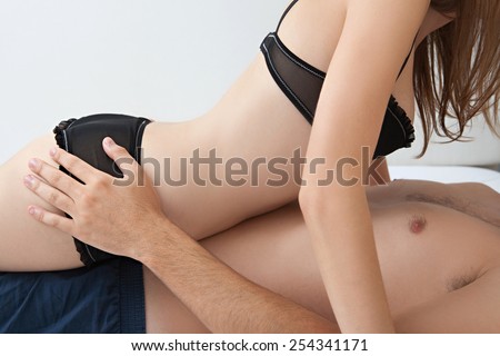 Side profile of a young lovers couple body section laying down together on a bed, with the girl laying on top of the man being playful and joyful indoors. Relationships lifestyle and sex life.