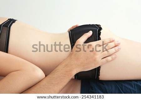 Side profile of a young lovers couple body section laying down together on a bed, with the girl laying on top of the man being playful indoors. Relationships lifestyle and sex life. Romance living.