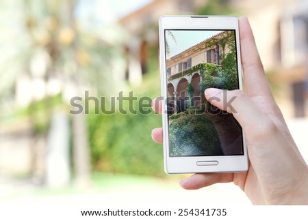 Close up detail view of a tourist woman hands holding a touch screen smartphone mobile cell device, to take holiday pictures of a building on vacation. Travel and lifestyle technology outdoors.