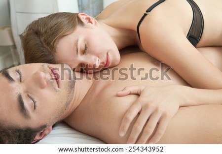 Close up portrait of an attractive young couple sleeping together while hugging on a white linen hotel bed, indoors. Couple and romance living lifestyle. Sensuality and relationships, home interior.