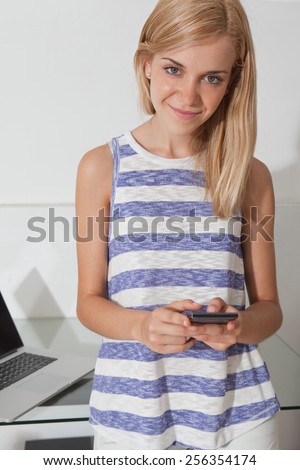Portrait of attractive teenager girl college student using smartphone technology and a laptop computer, against a white wall space working from home. Professional young woman using a mobile indoors.
