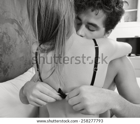 Portrait of young attractive romantic couple hugging and kissing, man undressing woman on a white bed, having sex and being loving with each other. Love and relationships lifestyle, interior bedroom.