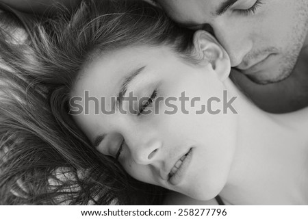 Black and white portrait of young attractive romantic couple hugging and kissing, laying down on a bed, having sex and being loving with each other. Love and relationships lifestyle, interior bedroom.
