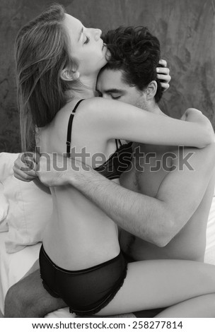 Black and white young attractive romantic couple hugging and kissing, man undressing woman on a white bed, having sex and loving each other. Love and relationships lifestyle, interior bedroom.