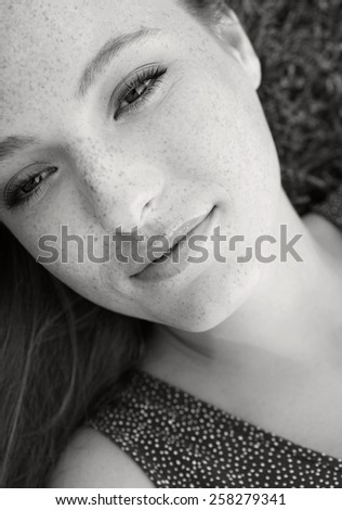Black and white beauty portrait of an attractive young beautiful tourist woman laying down on grass in a park, relaxing on a summer holiday, smiling. Healthy living and beauty lifestyle, exterior.