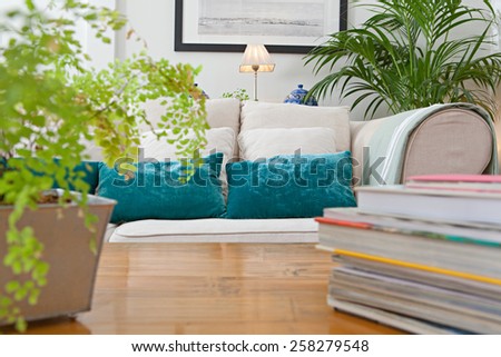 Interior design lifestyle of a home living room with white sofa and green cushions and plants, interior. House indoors with carpets and books on coffee table. Tranquil and aspirational home space.