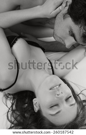 Black and white close up portrait of a young attractive couple hugging and kissing, together on a white bed, having sex and loving each other. Love and relationships lifestyle, interior bedroom.