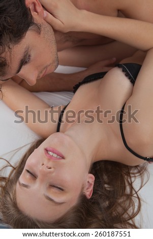 Close up portrait of a young attractive romantic couple hugging and kissing, laying down together on a white bed, having sex and loving each other. Love and relationships lifestyle, interior bedroom.