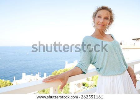 Beautiful portrait of a mature attractive woman relaxing in her holiday resort hotel balcony, contemplating the sea and blue sky on a summer vacation, outdoors. Beauty and lifestyle and well being.