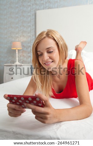 Portrait of attractive young teenager woman laying down relaxing in a stylish decorative home bedroom using a smartphone device to network and go on line. Home interior technology lifestyle, indoors.
