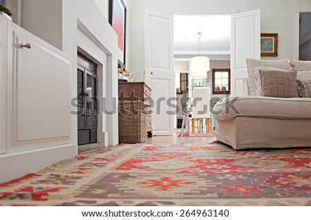 Still life of a stylish and luxurious home living room with sofa and a fireplace, and double wooden doors to a dining room, home interior with rugs and carpets. Aspirational living space, indoors.