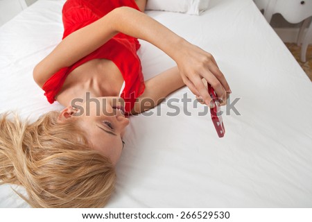 Attractive young teenager woman laying relaxing in stylish decorative home bedroom using a smartphone device touch screen to network on line. Home interior connectivity technology lifestyle, indoors.