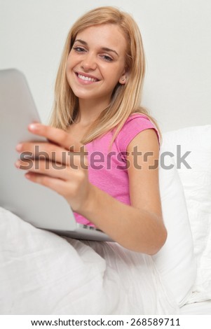 Portrait of beautiful teenager woman relaxing on bed in a bedroom with a laptop computer using technology and the internet, smiling indoors. Connectivity technology lifestyle, home bed room interior.