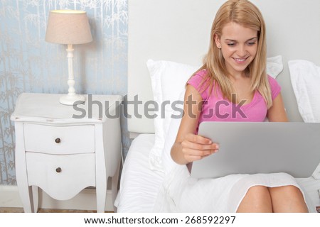 Portrait of beautiful teenager woman relaxing in a bedroom using a laptop computer using technology and the internet, smiling in house interior. Connectivity technology lifestyle, home interior.