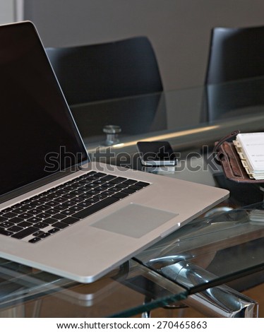 Still life office interior of an elegant meeting room with a glass desk and black chairs, technology laptop with blank screen and a smart phone, workplace interior. Indoors business office.