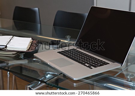 Still life office interior of an elegant meeting room with a glass desk and black chairs, technology open laptop with blank screen and a smart phone, workplace interior. Indoors business office.