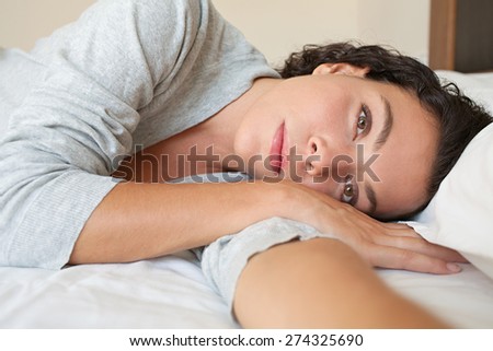 Portrait of a beautiful young exotic woman lounging relaxing on a bed at home, thoughtful wearing a robe, interior. Healthy wellness and well being home living aspirational lifestyle, bedroom indoors.