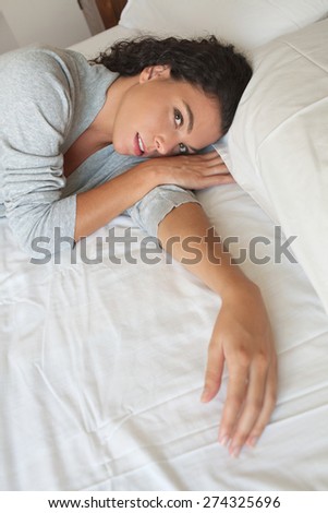 Portrait of a beautiful young exotic woman lounging relaxing on a bed at home, thoughtful wearing a robe, interior. Healthy wellness and well being home living aspirational lifestyle, bedroom indoors.