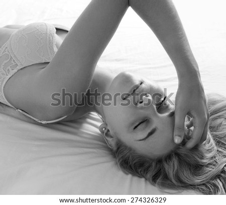 Black and white beauty portrait of young woman laying on a luxury bed in a home bedroom, with eyes shut, wearing sexy bra lingerie, hotel room, indoors. Home lifestyle and skin hair care, interior.