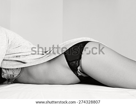 Black and white body figure faceless view of a beautiful young woman laying wearing sexy lingerie, relaxing on a bed at home, interior space. Well being aspirational lifestyle, bedroom indoors.