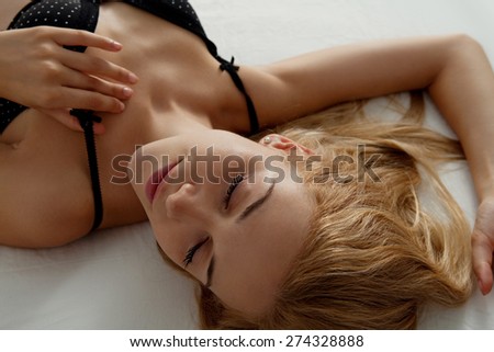 Over head close up beauty portrait of young woman laying relaxing on a bed at home bedroom, flirting wearing sexy black bra lingerie, hotel room, indoors. Home lifestyle and skin hair care, interior.