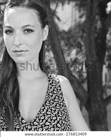 Black and white beauty portrait of a young attractive tourist woman on holiday, smiling, exterior. Travel and lifestyle during a sunny summer vacation break, outdoors. Beautiful woman with freckles.