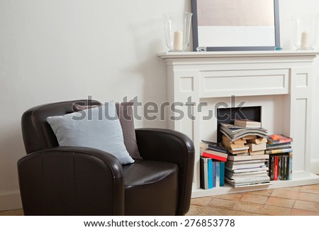 Still life interior design relaxing home reading room with comfortable quality leather armchair in a stylish house with fireplace. Aspirational home with books and cushions, indoors living lifestyle.