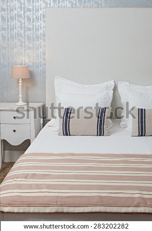 Still life of aspirational luxury home bedroom with stripy furnishings in a quality family home, interior design. Stylish bed with white linen and a pattern wallpaper with bamboo details, indoors.