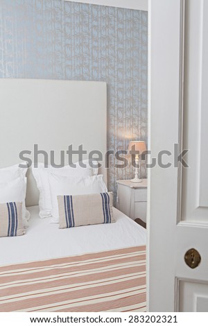 Still life of a luxury home bedroom with stripy furnishings in a quality family home, seen through a door ajar, semi open bedroom door, interior. Aspirational bedroom with pattern wallpaper indoors.