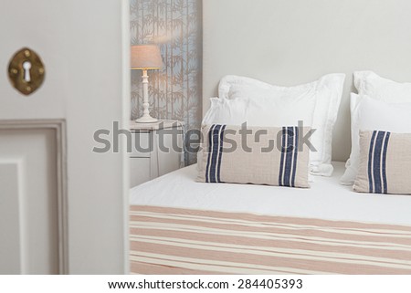 Still life of a luxury home bedroom in a quality family home, seen through a door ajar, semi open bedroom door, interior. Aspirational bed in home room with a bamboo pattern wallpaper indoors.