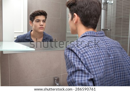 Portrait view of a young teenager man looking at himself in a home bathroom mirror, getting ready for school in the morning, home interior. Health and well being, male care and grooming, indoors.