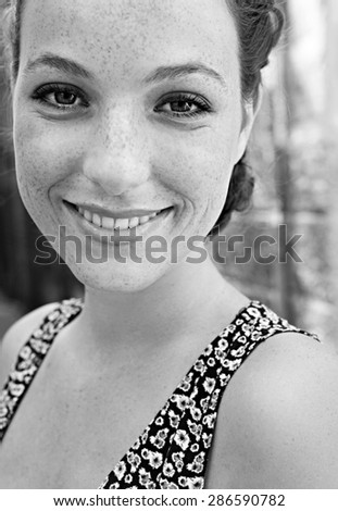 Black and white close up portrait of a young attractive tourist woman visiting a destination city while on a summer holiday, looking at camera and joyfully smiling, outdoors.