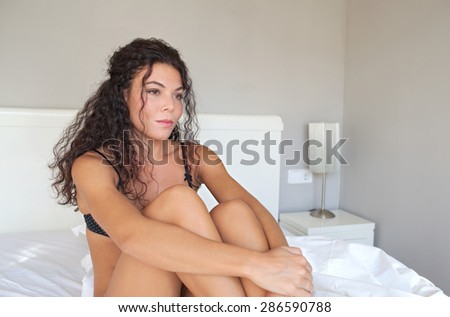Beauty body figure of young beautiful exotic sexy woman sitting on a bed at home in black lingerie, thoughtful and moody, relaxing on a bedroom, interior. Health well being and woman issues, indoors.