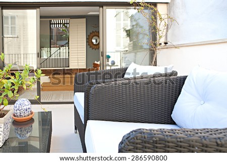 Still life view of a home outdoors living room and terrace sitting and relaxing area with a comfortable wicker sofa, in a stylish house, indoors and outdoors. Empty space, aspirational lifestyle.